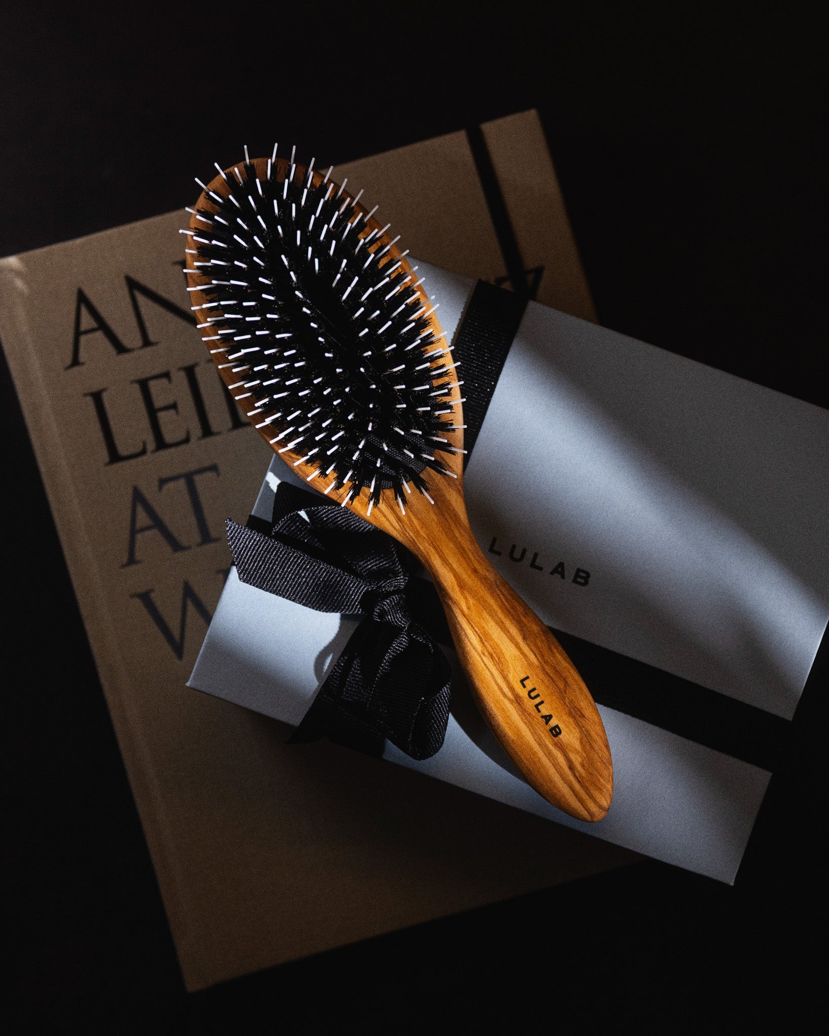 Træhårbørste med mørke naturbørster ligger på en gaveæske med sort bånd og LULAB emballage.