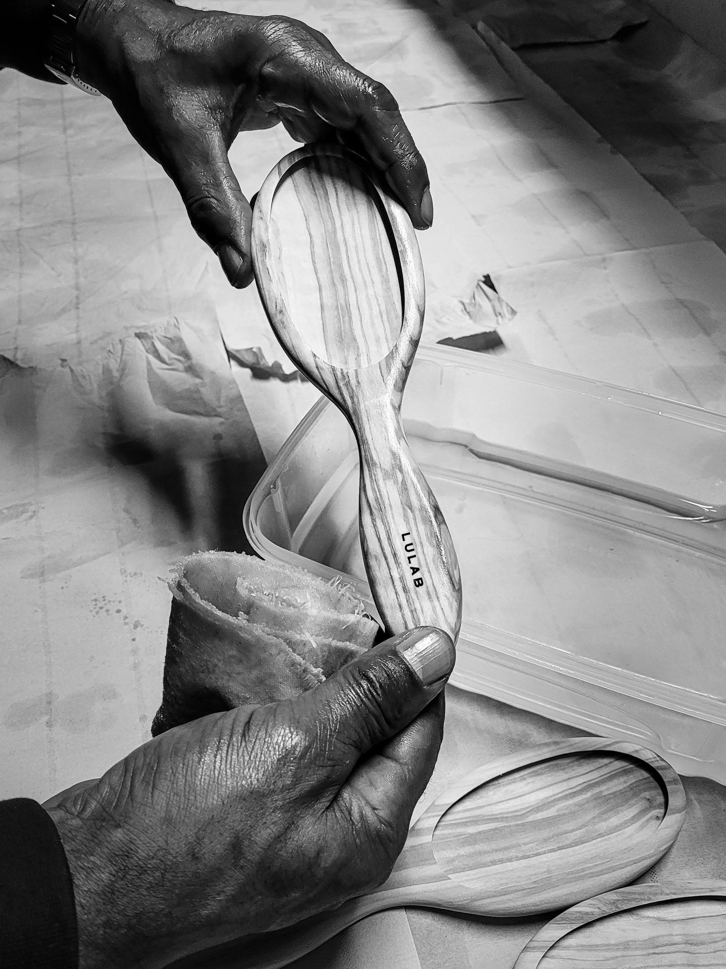 Sort-hvidt billede af hænder, der polerer og færdiggør en træhårbørste med en klud.