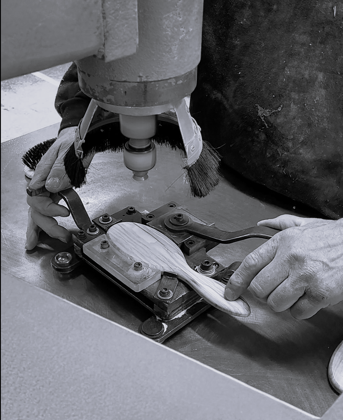 Sort-hvidt billede af en træhårbørste fastspændt i en maskine under præcis bearbejdning i produktionen.