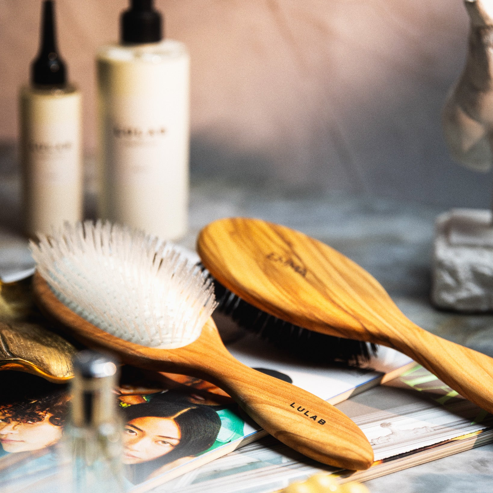 To træhårbørster med forskellige børstetyper ligger på et magasin omgivet af hårplejeprodukter.